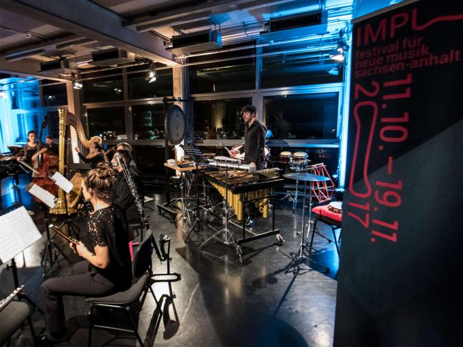 Ein junges Ensemble spielt vor einem Banner mit der Aufschrift „Impuls festival für neue musik sachsen-anhalt 11.10.–19.11.2017“