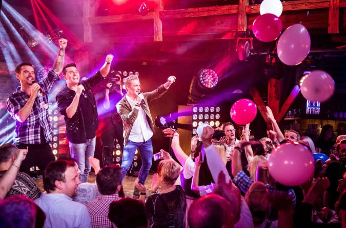 Drei Schlagersänger auf der Bühne während der „Hüttenparty“ im Mitteldeutschen Rundfunk 2019. Über das Publikum fliegen rosafrbene Luftballons