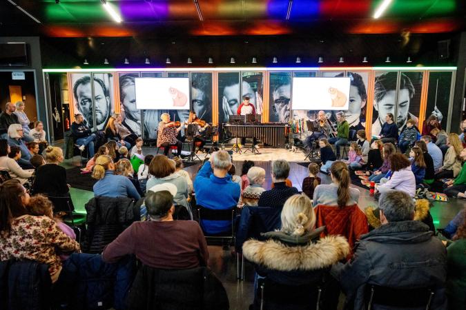 Gemischtes Ensemble auf einer Bühne, davor altersmäßig gemischtes Publikum