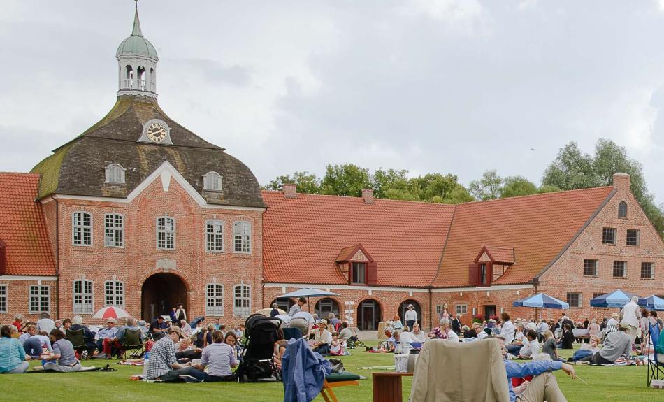 Menschen mit Campingstühlen und Sonnenschirmen vor Schloss mit roten Klinkermauern