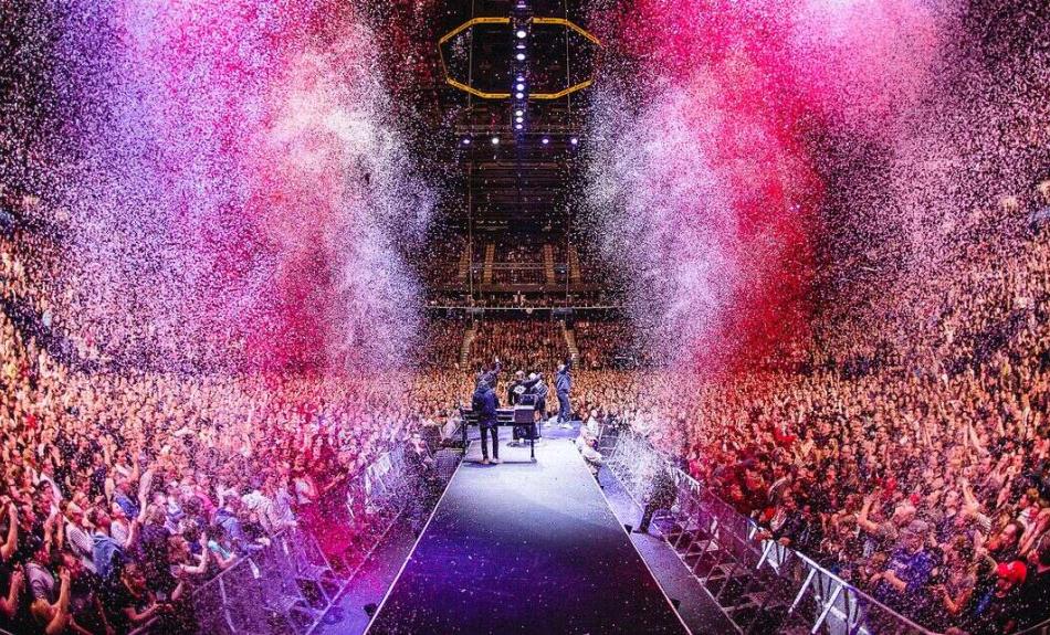 Die Hip-Hop-BAnd Die Fantastischen Vier stehen auf der Bühne, mit den Gesichtern zu einem riesigen Publikum. Links und rechts von der Bühne schießt rosafarbenes Confetti in die Höhe.