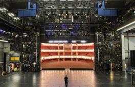 Eine Person steht auf einer Bühne und schaut in den halbrunden Zuschauerraum.