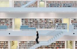 Ein heller Bibliotheksraum mit mehreren Ebenen, eine Frau geht eine Treppe herunter