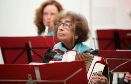 Eine alte Damen sitzt mit ihrem Akkordeon vor einem roten Notenständer.