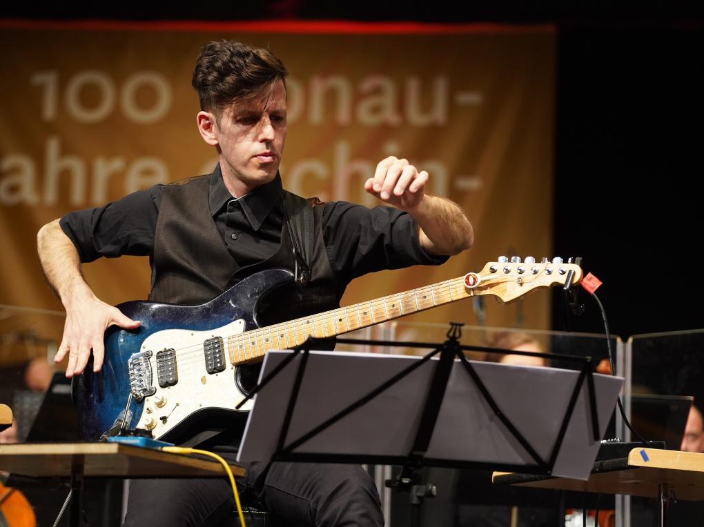 Gitarrist klopft auf seine E-Gitarre und zupft Saiten am Hals des Instruments