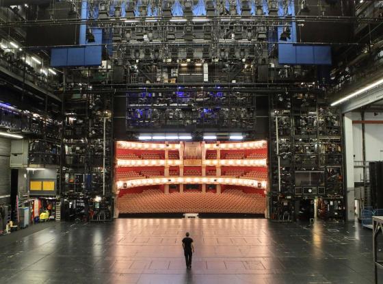 Eine Person steht auf einer Bühne und schaut in den halbrunden Zuschauerraum.