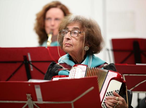 Eine alte Damen sitzt mit ihrem Akkordeon vor einem roten Notenständer.