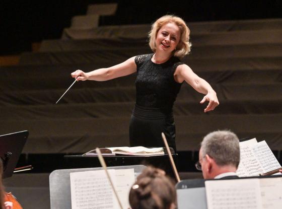 Eine blonde Frau dirigiert ein Orchester