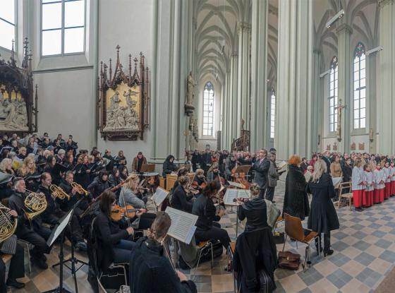 Links im Bild ein Orchester mit musikalischem Leiter und rechts im Bild die Gemeinde und Messdiener während eines Gottesdiensts in der Heilig-Kreuz-Kirche Giesing.